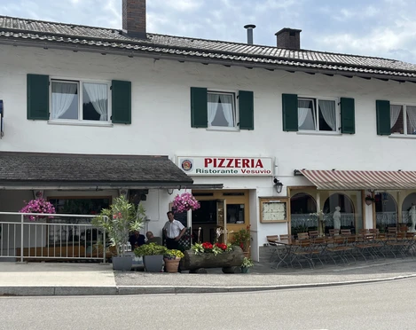 Pizzeria Ristorante Vesuvio - Außenansicht    Ein Wohnhaus mit einer Pizzeria im Erdgeschoss. Sitzmöglichkeiten vor dem Haus. Bunte Blumenkästen wirken einladend.