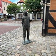 Calenberger Bur Bronzefigur eines historischen Arbeiters mit Schlägermütze auf gepflastertem Platz in Stadtkulisse.