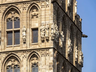 Historic town hall Die Fassade des Historischen Rathauses Köln zeigt detailreiche Figuren und gotische Architektur. Sonnenstrahlen heben die feinen Steinmetzarbeiten auf den sandfarbenen Türmen hervor. The façade of Cologne's historic town hall features detailed figures and Gothic architecture. The sun's rays highlight the fine stone carvings on the sand-colored towers.