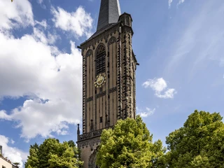 Saint Severin Sankt Severin in Köln zeigt sich auf dem Bild als majestätische Kirche mit einem hohen Turm, umgeben von grünen Bäumen und einem blauen Himmel.The picture shows St. Severin in Cologne as a majestic church with a high tower, surrounded by green trees and a blue sky.