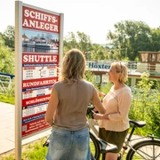 Hoexter-Schiffsanleger-Stadt Hoexter-D. Ketz-2023-254.jpg Zwei Frauen schauen interessiert auf den Fahrplan des Ausflugsschiffes an der WeserTwo women look with interest at the timetable of the excursion boat on the Weser
