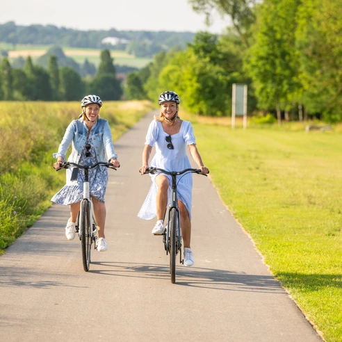 Hoexter-Freizeitanlage Godelheimer See-Stadt Hoexter-D. Ketz-2023-219.jpg Zwei Frauen radeln auf dem Weser-Radweg entlang eines Badesees