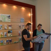 Tourist Info Zwei Personen betrachten in einem Informationszentrum Karten und Prospekte an einer beleuchteten Wand.