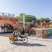 Moritzbastei - Veranstaltungen in Leipzig Bild vom oberen Eingang zur Moritzbastei am Kurt-Masur-Platz in Leipzig, in der es ein Café und Restaurant gibt und in dem viele Veranstaltungen stattfinden, eine Fahrradfahrerin fährt durch das Bild