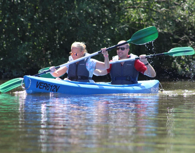 Kanutour Ein Mann und eine Frau paddeln in einem blauen Kanu durch ein ruhiges Gewässer, umgeben von grüner Natur.