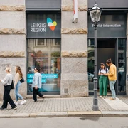 Eingang zur Tourist-Information Leipzig - Besucherberatung und Service Fassade und Haupteingang der Tourist-Information Leipzig in der Katharinenstraße 8, einige Touristen stehen vor dem Eingang und schauen sich Informationsmaterial anFasada i wejście główne do Informacji Turystycznej w Lipsku na Katharinenstraße 8, kilkoro turystów stoi przed wejściem i przygląda się materiałom informacyjnymThe façade and main entrance of the Leipzig Tourist Information Office, Katharinenstraße 8. Several tourists are standing in front of the entrance and looking at informational materialFaçade et entrée principale de l'office de tourisme de Leipzig au 8 rue Katharinenstraße, quelques touristes se tiennent devant l'entrée et consultent de la documentationFasáda a hlavní vchod do turistického informačního centra v ulici Katharinenstraße 8, před vchodem stojí několik turistů prohlížejících si informační materiál