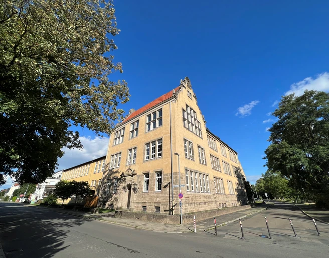Albert Schweizer-Schule Dreistöckiges historisches Schulgebäude mit gelber Fassade und markantem Giebel unter blauem Himmel.
