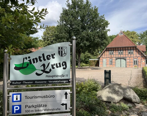 Der Lintler Krug ist ein traditionelles Backsteingebäude mit begrüntem Vorplatz und großem Baum.