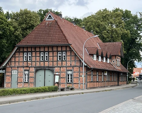 Das Fachwerkgebäude Lintler Krug mit rotem Ziegeldach liegt an einer ruhigen Straße in grüner Umgebung.