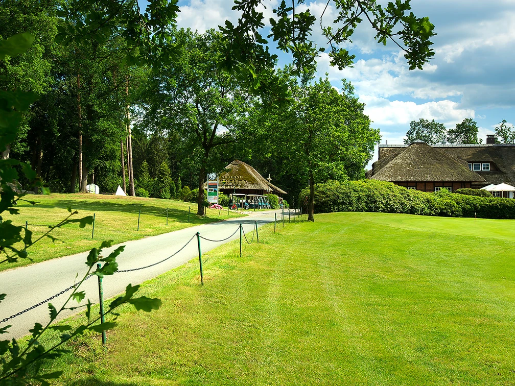 artland-golfclub Weg führt zu einem reetgedeckten Clubhaus im Artland Golfclub, umgeben von grüner Landschaft.