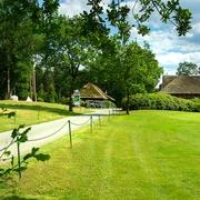 artland-golfclub Weg führt zu einem reetgedeckten Clubhaus im Artland Golfclub, umgeben von grüner Landschaft.