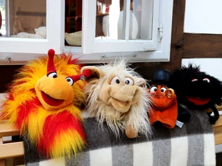 Tuchmacher Museum Bramsche im Osnabrücker Land Vier bunte Stofftiere sitzen lächelnd auf einer Holzbank vor einem Fachwerkhausfenster.