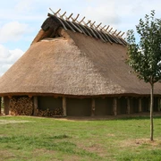 Das Eisenzeithaus in Ostercappeln-Venne Het huis van de ijzertijd in Ostercappeln-Venne is een woonstal nagebouwd uit de pre-Romeinse ijzertijd met eromheen een tuin met vergeten kruidenHistorisches Langhaus mit Reetdach auf einer Wiese, umgeben von Natur und Besuchern.