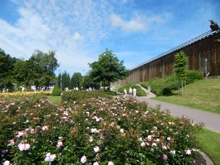 Gradeerwerk Bad Rothenfelde Mensen wandelen langs de grote gradeerwerken in Bad Rothenfelde en ademen zo de zuivere lucht met verneveld zout water in, wat lichte infecties van de luchtwegen verlicht.Blumenbeet mit Rosen, Spazierweg und Gradierwerk im Kurpark Bad Rothenfelde unter blauem Himmel.