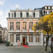 Das Couven-Museum, auf der Ecke eines gepflasterten Platzes, mit hellem rotem Anstrich, großen Sprossenfenstern und einem roten Teppich am Eingang.