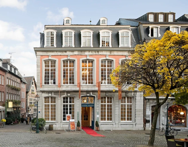 Couven Museum Das Couven-Museum, auf der Ecke eines gepflasterten Platzes, mit hellem rotem Anstrich, großen Sprossenfenstern und einem roten Teppich am Eingang.