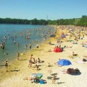 Dürener Badesee Strand Sandstrand mit vielen Besuchenden, die teils im See sind und teils am Ufer mit Sonnenschirmen liegen.