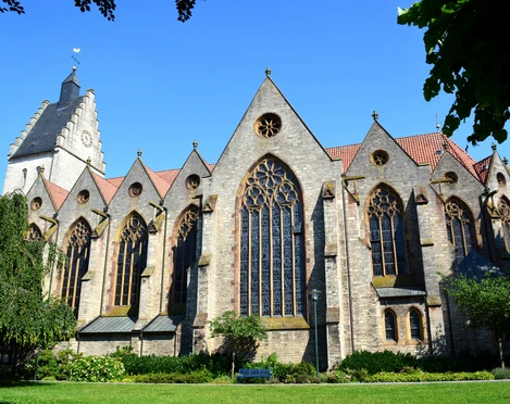 De Griese Toarn en de parochiekerk Mariae Geburt zijn bezienswaardigheden in Bad Laer in het Osnabrücker LandGotische Backsteinkirche mit großen Buntglasfenstern und grünem Garten im Vordergrund.