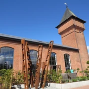 Eisenhütte Backsteinindustriegebäude mit Turm und großen Fenstern vor klarem Himmel; moderne Kunstinstallation vorne.