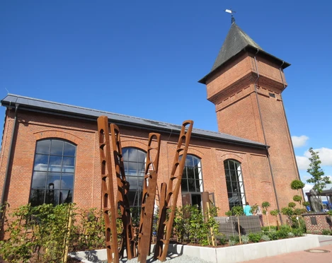Eisenhütte Backsteinindustriegebäude mit Turm und großen Fenstern vor klarem Himmel; moderne Kunstinstallation vorne.