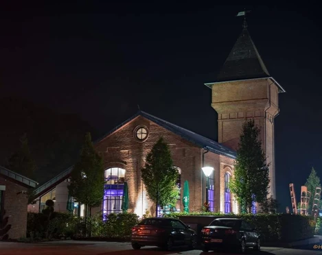 Eisenhütte bei Nacht Bei Nacht beleuchtete historische Eisenhütte mit markantem Turm vor dunklem Himmel.