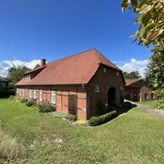 Müllerhaus Historisches Backsteinhaus mit rotem Satteldach, umgeben von grüner Wiese, unter blauem Himmel.