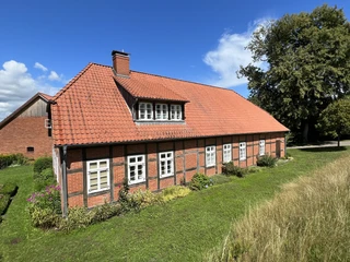 Altes Müllerhaus mit rotem Ziegeldach, Fachwerkdetails und umgeben von grüner Natur.