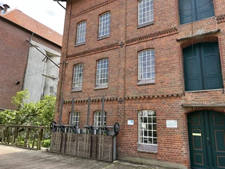 Wassermühle Stemmen Backsteingebäude einer historischen Mühle mit großen Fenstern und Details, flankiert von grüner Vegetation.