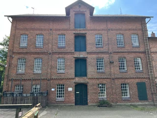 Wassermühle Stemmen Backstein-Wassermühle mit grünen Türen und Fenstern, in einem flachen, gepflasterten Vorhof.