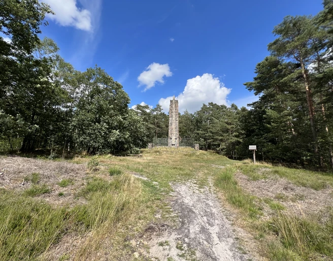 Lindhoopdenkmal Langer Gedenkstein umgeben von Wiese und Bäumen unter strahlend blauem Himmel mit weißen Wolken.