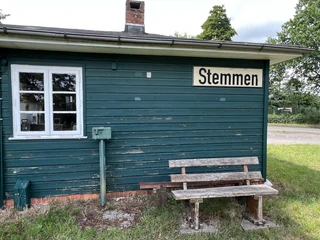 Alter Holzbahnhof in Stemmen, Niedersachsen, mit grüner Holzverkleidung und einer Holzbank außen.