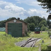 Verden-Stemmen Ein alter Güterschuppen mit grünen Toren und Uhr, daneben ein Schienenweg mit einer historischen Lokomotive.