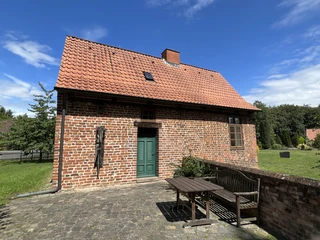 Kapitelhaus Wittlohe Backsteingebäude mit rotem Ziegeldach und grüner Holztür, umgeben von gepflastertem Boden und Garten.