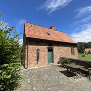 Kapitelhaus Wittlohe Rotes Ziegelhaus mit rotem Satteldach und grüner Tür, umgeben von einem gepflasterten Hof und Bäumen.