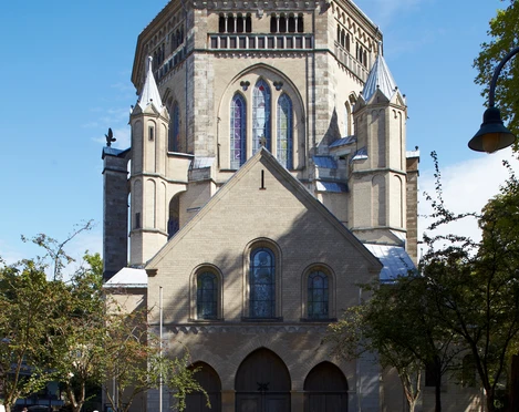 Saint Gereon Romanische Kirche aus Sandstein mit imposanter Kuppel und Buntglasfenstern, umgeben von Bäumen.Romanesque church made of sandstone with an imposing dome and stained glass windows, surrounded by trees.