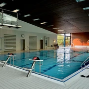 Gartenhallenbad innen Schwimmhalle mit großem Becken, Rettungssteg und Leiter, helles Interieur mit bunter Wandgestaltung.