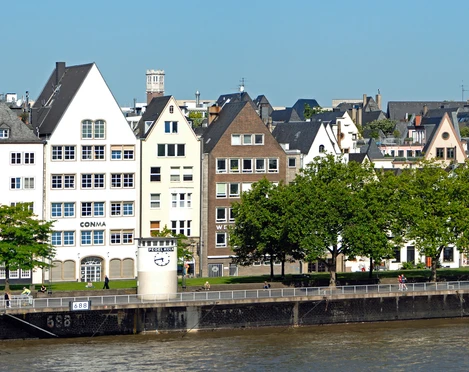 Pegel Köln Reihen schiefer Fachwerkhäuser mit spitzen Dächern säumen das Rheinufer unter strahlend blauem Himmel.Rows of crooked half-timbered houses with pointed roofs line the banks of the Rhine under a bright blue sky.