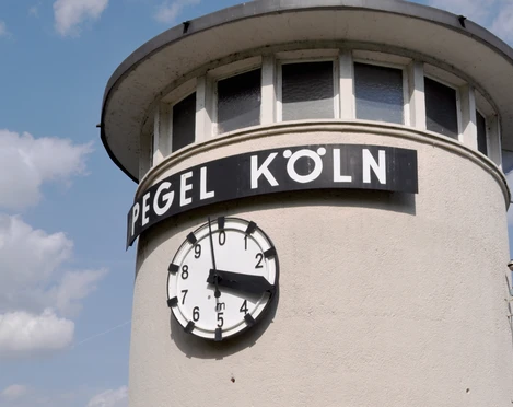 Water level Cologne Runder Pegelturm in Köln mit weißer Fassade und schwarzer Uhr, die drei Uhr zeigt.Round water gauge tower in Cologne with white façade and black clock showing three o'clock.