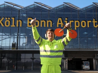 Köln Bonn Airport Mitarbeiter in leuchtender Jacke gibt mit Signalgeräten Gesten vor dem Köln Bonn Airport.Employee in bright jacket gestures with signaling devices in front of Cologne Bonn Airport.