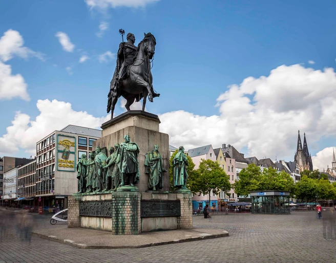 Equestrian statue of King Frederick William III. Denkmal des preußischen Königs auf einem Pferd, umringt von Statuen in belebter Altstadt mit Domblick.Monument to the Prussian king on a horse, surrounded by statues in a lively old town with a view of the cathedral.