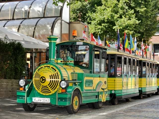 Wolters Bimmelbahn Das Bild zeigt eine fröhlich gestaltete Bimmelbahn mit bunten Flaggen auf ihrem Dach, geparkt an einem sonnigen Bürgersteig.The picture shows a cheerfully designed Bimmelbahn with colorful flags on its roof, parked on a sunny sidewalk.