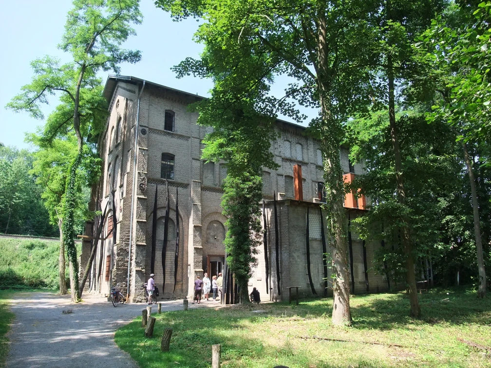 Gedenkstätte Augustaschacht, umgeben von Bäumen, mit einem historischen Backsteingebäude im Hintergrund.
