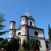 Romanische Marienkapelle mit weißem Mauerwerk und kunstvollen Türmen, von Grün umgeben.