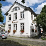 Kornelimünster Weißes, zweistöckiges Gebäude mit dekorativen Blumen, umrahmt von alten Bäumen.