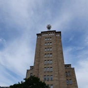 Wettersäule  Auf einem hohen, turmähnlichen Gebäude mit Fenstern steht eine Wetterstation mit runder Kuppel unter leicht bewölktem Himmel..