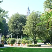 Burtscheid Park mit der Außenterrasse eines Lokals und einer Kirchturmspitze hinter Baumkronen.