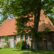 bispingen-ole-kerk Die alte Kirche in Bispingen aus Feld- und Backsteinen mit rotgedecktem Satteldach, umgeben von Grün.