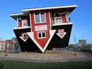 das-verrueckte-haus-bispingen Bild zeigt ein rotes, kopfstehendes Haus in Bispingen unter blauem Himmel.