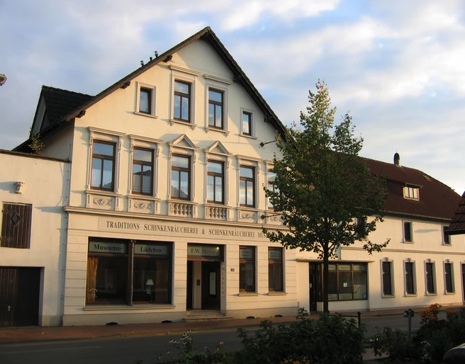 Schinkenmuseum-Apen Das Bild zeigt ein traditionelles Gebäude mit einem Schild, das "Traditions-Schinkenräucherei & Schinkenmuseum" anzeigt.