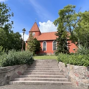 St. Petri-Kirche Kirchlinteln Die St. Petri-Kirche in Kirchlinteln mit roter Fassade, umgeben von Bäumen und eingebettetem Treppenaufgang.